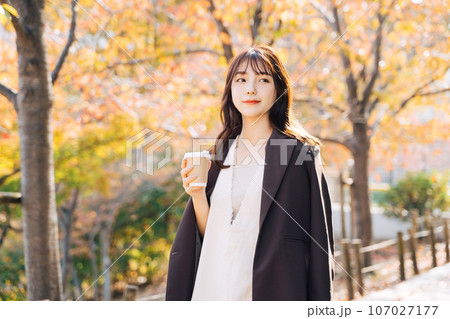 紅葉の季節に屋外でコーヒーを飲む女性 107027177