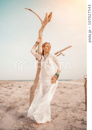 woman sea white dress. Model in boho style in a white long dress and silver jewelry on the beach. Her hair is braided, and there are many bracelets on her arms. woman sea white dress. Model in boho style in a white long dress and silver jewelry on the beach. Her hair is braided, and there are many bracelets on her arms. 107027543