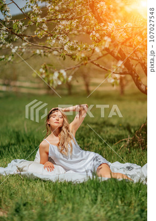 woman garden. she sleeps on a white bed in the fresh spring grass in the garden. Dressed in a blue nightgown. 107027548