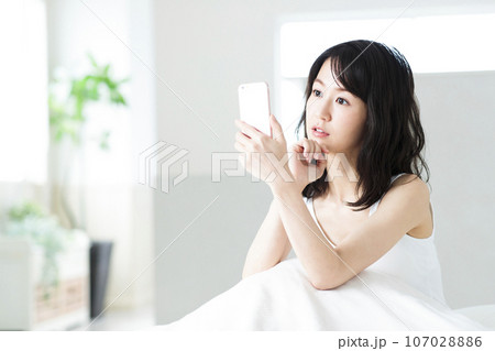 ベッドルームでスマホを見る若い女性 107028886