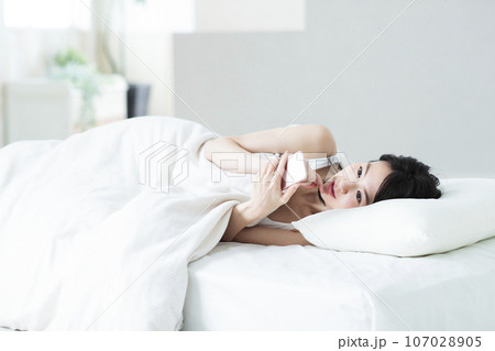 ベッドの中でスマホを操作する若い女性 107028905
