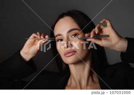 beautiful woman holding eyelashes tweezers on black background 107031000