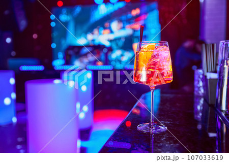 Alcoholic cocktail with ice and a piece of orange on the bar counter Alcoholic cocktail with ice and a piece of orange on the bar counter 107033619