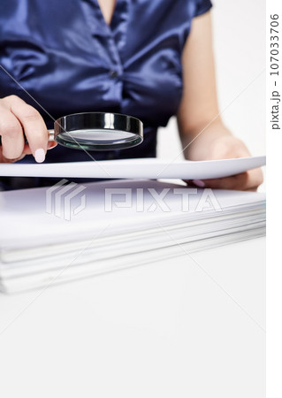 An office worker examines documents through a magnifying glass An office worker examines documents through a magnifying glass 107033706