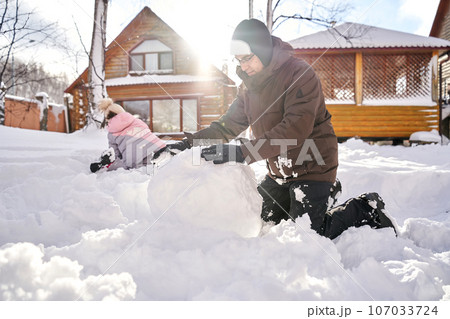 A family builds a snowman out of snow in the yard in winter. 107033724