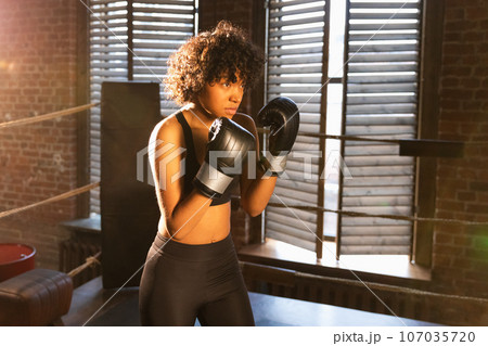 Outcry independent girl power. Angry african american woman fighter with boxing gloves looking serious aggressive standing on boxing ring. Strong powerful fighter girl training punches Outcry independent girl power. Angry african american woman fighter with boxing gloves looking serious aggressive standing on boxing ring. Strong powerful fighter girl training punches 107035720