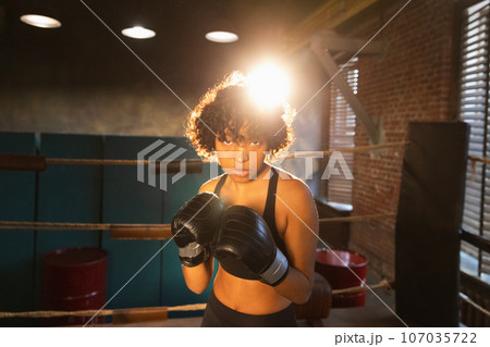 Outcry independent girl power. Angry african american woman fighter with boxing gloves looking serious aggressive standing on boxing ring. Strong powerful fighter girl training punches Outcry independent girl power. Angry african american woman fighter with boxing gloves looking serious aggressive standing on boxing ring. Strong powerful fighter girl training punches 107035722