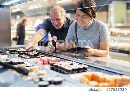 Couple chooses sushi near refrigerator in supermarket 107036520