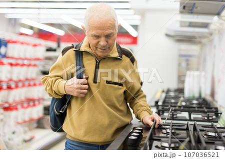 Senor man pensioner buying kitchen stove in showroom of electrical appliance store 107036521