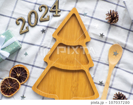 Empty christmas tree shaped wooden plate with 2024 and spoon on towel background 107037280