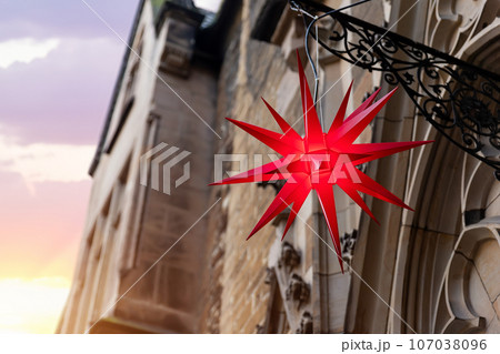 Beautiful Moravian star or Herrnhuter Stern street glowing decoration hanged on wall german city street at christmas advent winter holidays. Traditional Xmas ornament decor in Germany 107038096