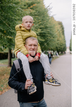 Dad holds on his son's shoulders. Beautiful family is spending time together outside. Dad and his little son are having fun on a roof terrace with view on a city. Sitting on father's shoulders and 107038392