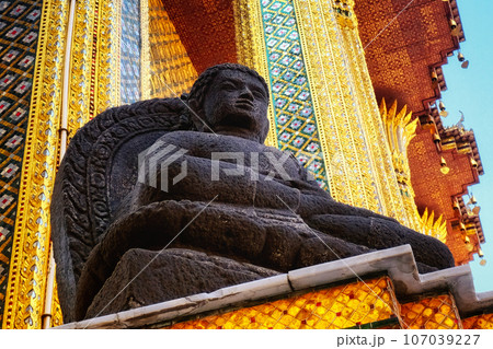 A contemplative Buddha statue within a temple. The black statue, in repose on a stand, is set against an energetic background of ornate designs in gold, verdant, and cyan. A contemplative Buddha statue within a temple. The black statue, in repose on a stand, is set against an energetic background of ornate designs in gold, verdant, and cyan. 107039227