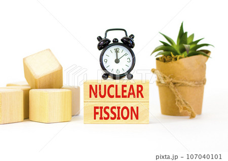 Nuclear fission symbol. Concept words Nuclear fission on beautiful wooden blocks. Beautiful white table white background. Black alarm clock. Business science nuclear fission concept. Copy space. 107040101