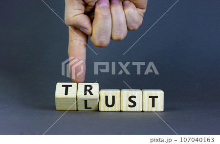 Lust or trust symbol. Businessman turns wooden cubes and changes the words 'lust' to 'trust'. Beautiful grey table, grey background. Business and lust or trust concept, copy space. Lust or trust symbol. Businessman turns wooden cubes and changes the words 'lust' to 'trust'. Beautiful grey table, grey background. Business and lust or trust concept, copy space. 107040163