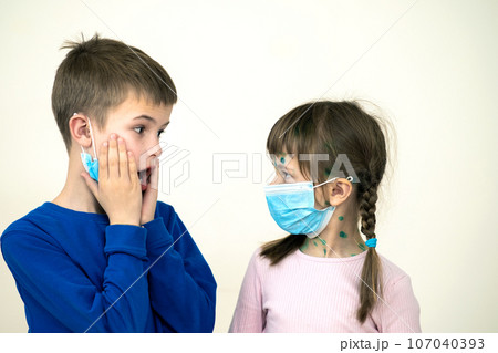 Boy and girl wearing blue protective medical mask ill with chickenpox, measles or rubella virus with rashes on body. Children protection during epidemic of coronovirus. Covid-19 contagion concept. Boy and girl wearing blue protective medical mask ill with chickenpox, measles or rubella virus with rashes on body. Children protection during epidemic of coronovirus. Covid-19 contagion concept. 107040393