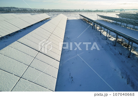 Aerial view of snow covered sustainable electric power plant with rows of solar photovoltaic panels for producing clean electrical energy. Low effectivity of renewable electricity in northern winter 107040668