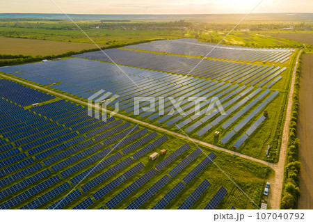 Aerial view of large electrical power plant with many rows of solar photovoltaic panels for producing clean ecological electric energy at sunrise. Renewable electricity with zero emission concept Aerial view of large electrical power plant with many rows of solar photovoltaic panels for producing clean ecological electric energy at sunrise. Renewable electricity with zero emission concept 107040792