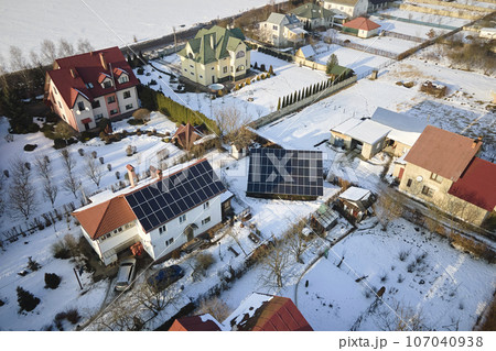 Aerial view of house roof with solar panels covered with snow melting down in winter end for producing clean energy. Concept of low effectivity of renewable electricity in northern region 107040938