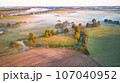 Warm sunny September morning. Autumn beautiful fog landscape. Small river curves in trees. Bright sunny misty riverside. Scenic view of rural sunrise. Village in Agriculture fields 107040952