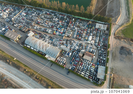Aerial view of big parking lot of junkyard with rows of discarded broken cars. Recycling of old vehicles Aerial view of big parking lot of junkyard with rows of discarded broken cars. Recycling of old vehicles 107041069