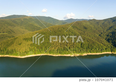 Aerial view of big lake with clear blue water between high mountain hills covered with dense evergreen forest. Aerial view of big lake with clear blue water between high mountain hills covered with dense evergreen forest. 107041071