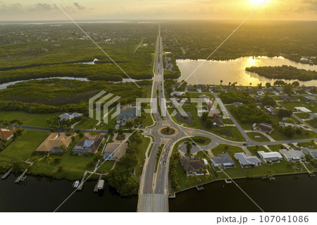 Aerial view of american suburban area with rural road roundabout intersection with moving cars traffic. Circular transportation crossroads in Florida Aerial view of american suburban area with rural road roundabout intersection with moving cars traffic. Circular transportation crossroads in Florida 107041086