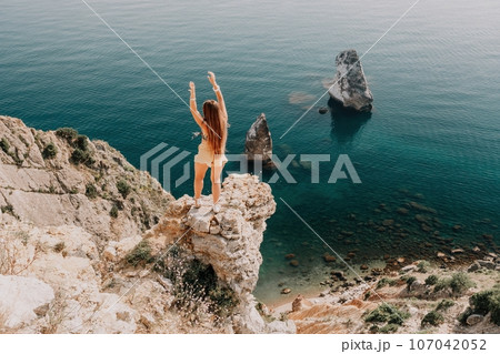 Woman travel sea. Happy tourist enjoy taking picture outdoors for memories. Woman traveler looks at the edge of the cliff on the sea bay of mountains, sharing travel adventure journey Woman travel sea. Happy tourist enjoy taking picture outdoors for memories. Woman traveler looks at the edge of the cliff on the sea bay of mountains, sharing travel adventure journey 107042052