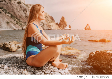 Woman sea yoga. Happy woman meditating in yoga pose on the beach, ocean and rock mountains. Motivation and inspirational fit and exercising. Healthy lifestyle outdoors in nature, fitness concept. Woman sea yoga. Happy woman meditating in yoga pose on the beach, ocean and rock mountains. Motivation and inspirational fit and exercising. Healthy lifestyle outdoors in nature, fitness concept. 107046959