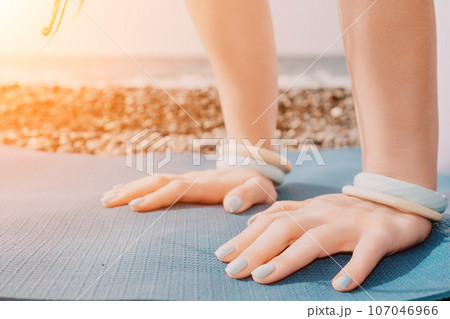 Woman sea yoga. Well looking middle aged woman with braids dreadlocks in white leggings and tops doing stretching pilates on yoga mat near sea. Female fitness yoga routine concept. Healthy lifestyle. 107046966