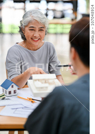 A happy and satisfied Asian retired lady is having a meeting with her architect or interior designer A happy and satisfied Asian retired lady is having a meeting with her architect or interior designer 107048914