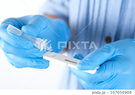 The doctor holds a COVID-19 swab collection, wears blue gloves and a PPE protective mask, and carries a test tube to collect the OP NP and test coronavirus. 107050909
