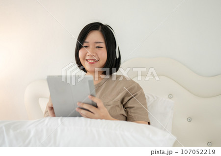 A beautiful and happy Asian plus-size woman enjoys watching videos online on her tablet on bed. A beautiful and happy Asian plus-size woman enjoys watching videos online on her tablet on bed. 107052219