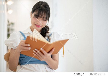 A beautiful and happy Asian woman enjoys reading a book while relaxing in a coffee shop. A beautiful and happy Asian woman enjoys reading a book while relaxing in a coffee shop. 107052287