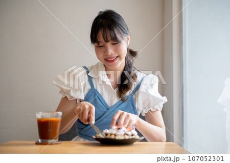 A pretty Asian woman enjoys eating a croissant waffle and an iced coffee in a coffee shop alone. 107052301