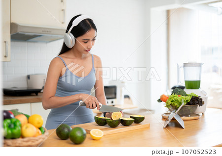 A healthy Asian woman is listening to music while preparing her breakfast in the kitchen. A healthy Asian woman is listening to music while preparing her breakfast in the kitchen. 107052523
