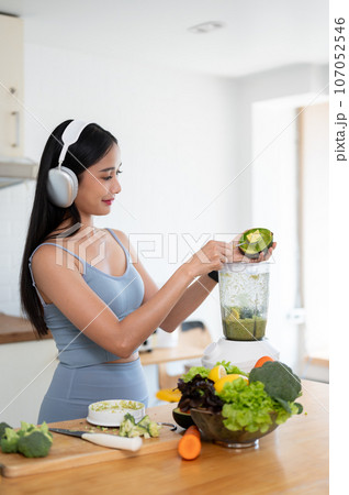 A slim Asian woman in gym clothes and headphones is making her healthy green smoothie. 107052546