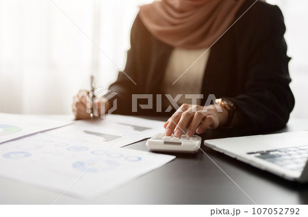 A professional Muslim or Arab businesswoman is analyzing business financial data on reports. A professional Muslim or Arab businesswoman is analyzing business financial data on reports. 107052792