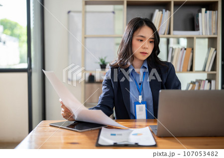 A serious and focused Asian businesswoman is working on her assignment on her laptop at her desk. 107053482