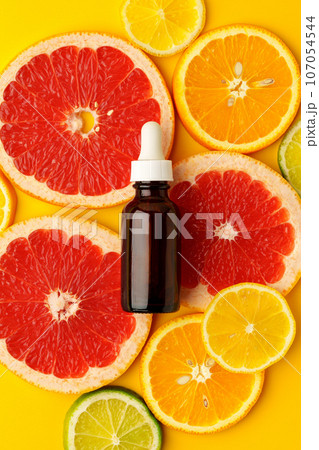 Citrus essential oil bottle on yellow background with sliced citrus fruits top view 107054544