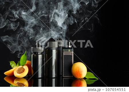 Vape and smoking liquid with fruit against black background with smoke 107054551