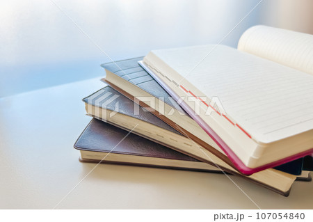 窓辺に積み上げられた古い日記帳と、まだ書かれていないページ 107054840