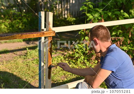 A person in the open air with a brush in his hand paints wood with varnish or stain. 107055281