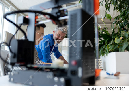 Two men architects using 3D printer in office and projecting house, drawing blueprints. Two men architects using 3D printer in office and projecting house, drawing blueprints. 107055503