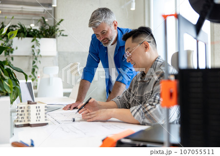 Men working with 3D printer and blueprint for designing mechanical parts in high tech workshop. Men working with 3D printer and blueprint for designing mechanical parts in high tech workshop. 107055511