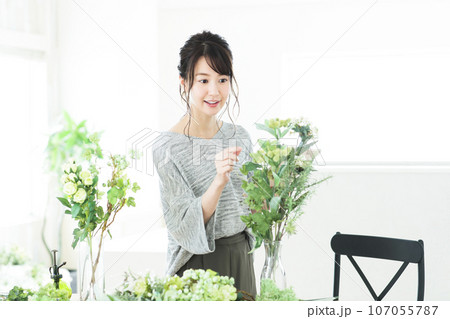 タブレットを操作しながらリビングでフラワーアレンジメントをする若い女性 タブレットを操作しながらリビングでフラワーアレンジメントをする若い女性 107055787