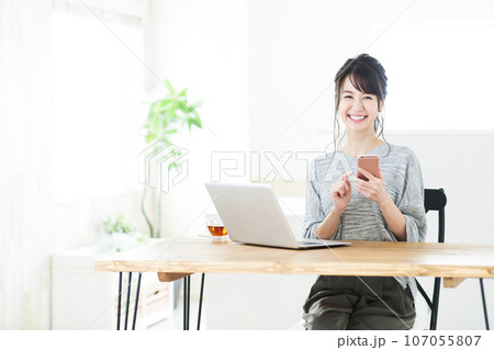 リビングでスマホとパソコンを操作する若い女性 107055807