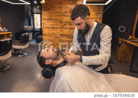 Caucasian man getting perfect shape of beard at barbershop. Caucasian man getting perfect shape of beard at barbershop. 107056028