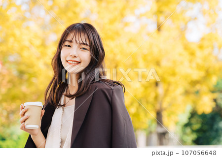 銀杏の木の下でコーヒーを飲む女性 107056648