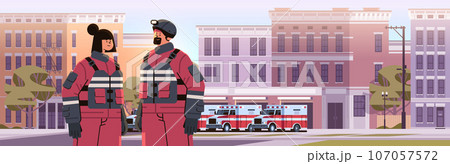 firefighters in uniform standing near fire station building department house facade and red emergency vehicles firefighters in uniform standing near fire station building department house facade and red emergency vehicles 107057572